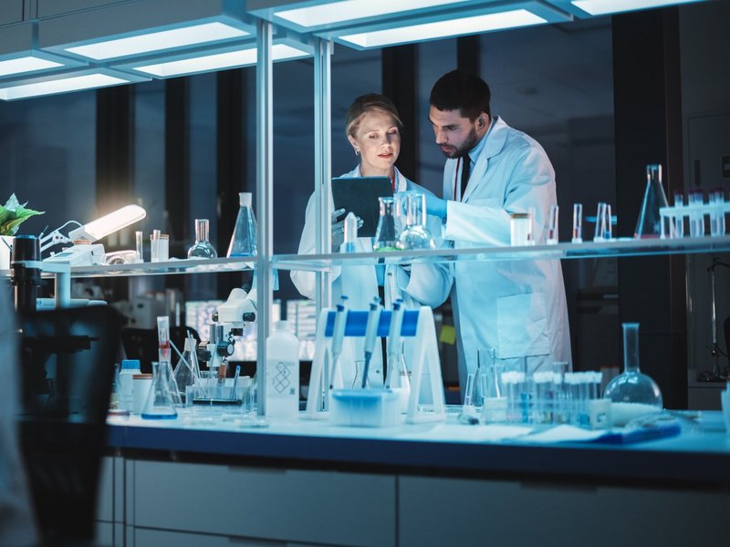 Female and Male Medical Research Scientists Have a Conversation While Conducting Experiments in a Petri Dish, Writing Analysis Results on a Tablet Computer. Modern Biological Science Laboratory.